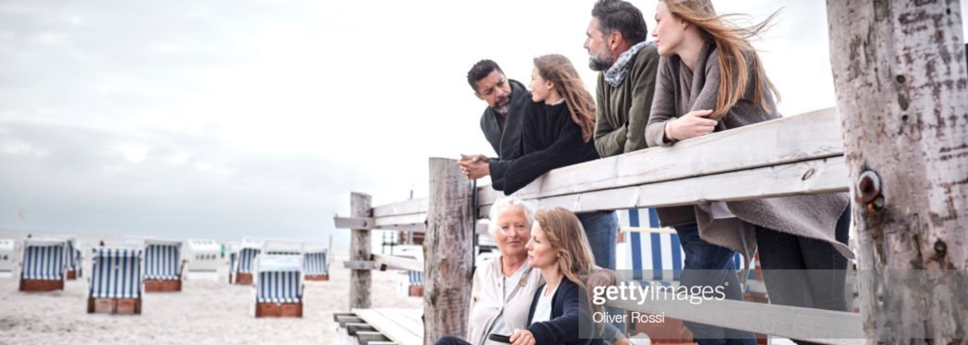 Family sitting and standing on pier looking out at the beach and ocean